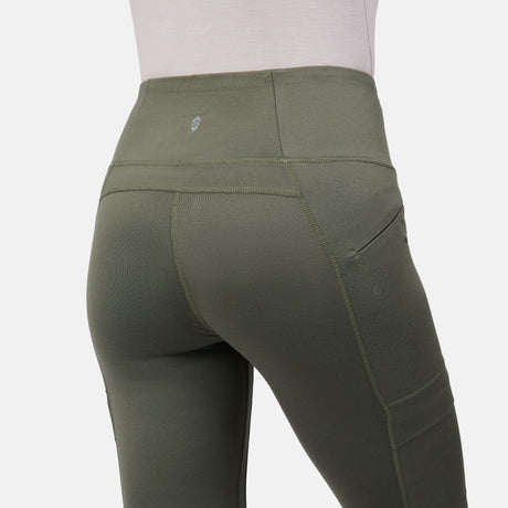 A person is shown from the back wearing Free Country Women’s Trail 2 Town Legging in olive green, featuring a high-rise waistband with a small logo, visible seams, and side pockets, set against a plain white background.