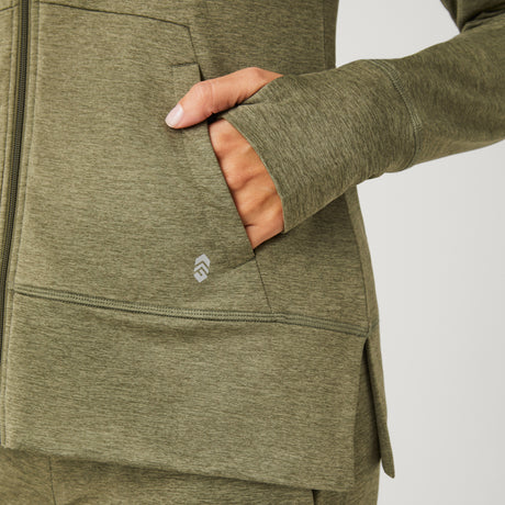 A close-up of someone wearing the Clearance Women's Free 2 Go Out Zip Hoodie in olive green, featuring a thumbhole sleeve and small logo by the pocket, styled effortlessly with four-way stretch shorts.
