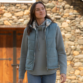 Woman wearing the Free Country Women's Venture Stratus Lite Reversible Vest in light blue, featuring a geometric-print Butter Pile® lining and horizontal quilted overlay
