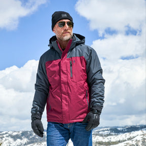 A man stands outdoors against snowy mountains and a partly cloudy sky, wearing the Clearance Men's Arvon Insulated Jacket in red and gray, paired with sunglasses, a black beanie, and gloves.