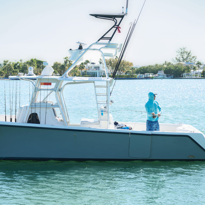 Man fishing on a large boat in clear water with trees in the background