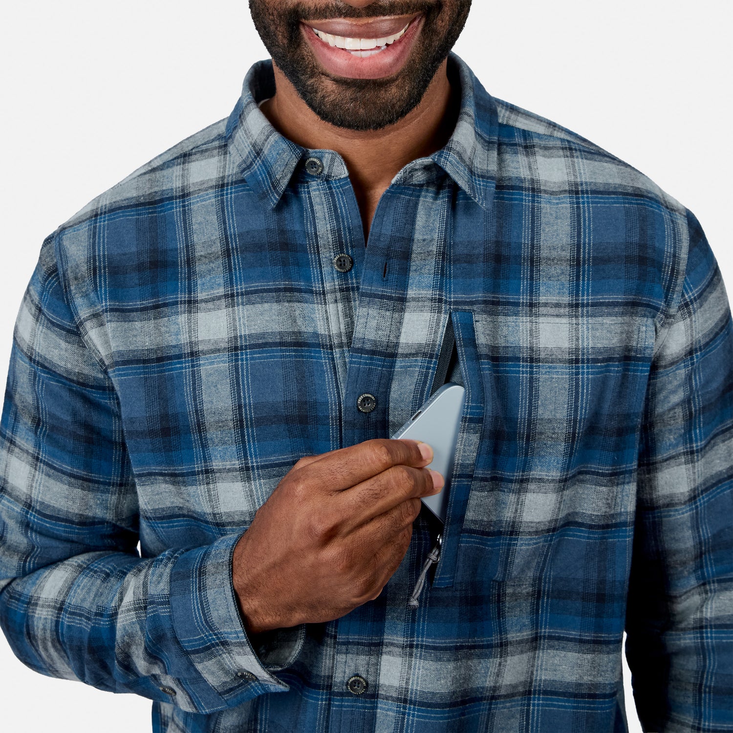 [Model is wearing size M.] Front view of a man in the blue plaid fleece lined flannel shirt smiling while holding a smartphone in the chest pocket