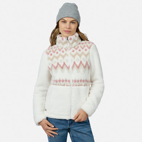 A woman in a gray beanie and blue jeans models the Free Country Women’s Sierra Butter Pile® Zip Up Jacket in Alpine Aztec Tearose against a plain white background.