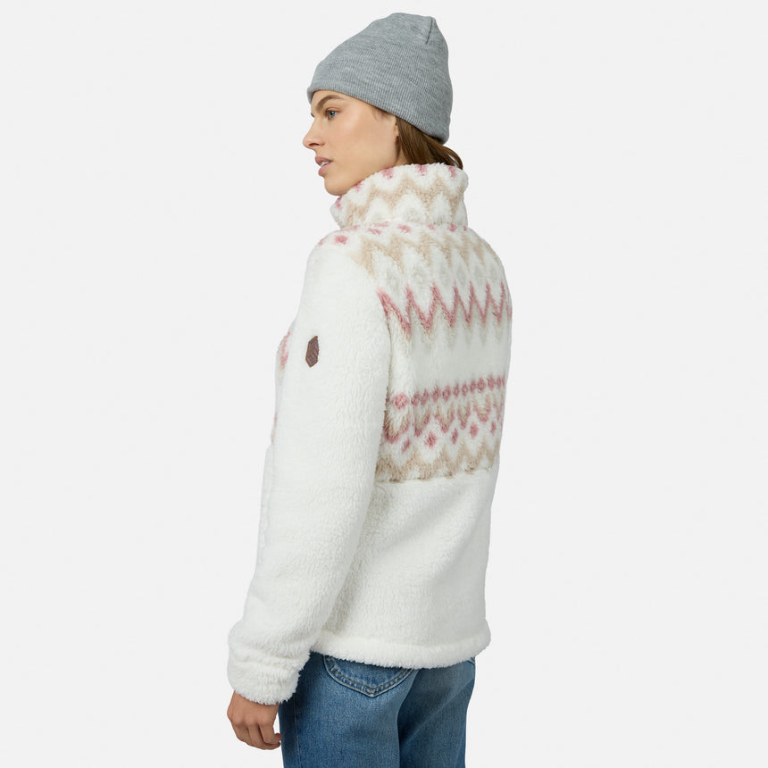 A woman in a gray beanie and blue jeans wears the Free Country Women’s Sierra Butter Pile® Zip Up Jacket—white with pink and beige geometric details—against a white background, looking to the side. Ideal lightweight warmth for chilly days.