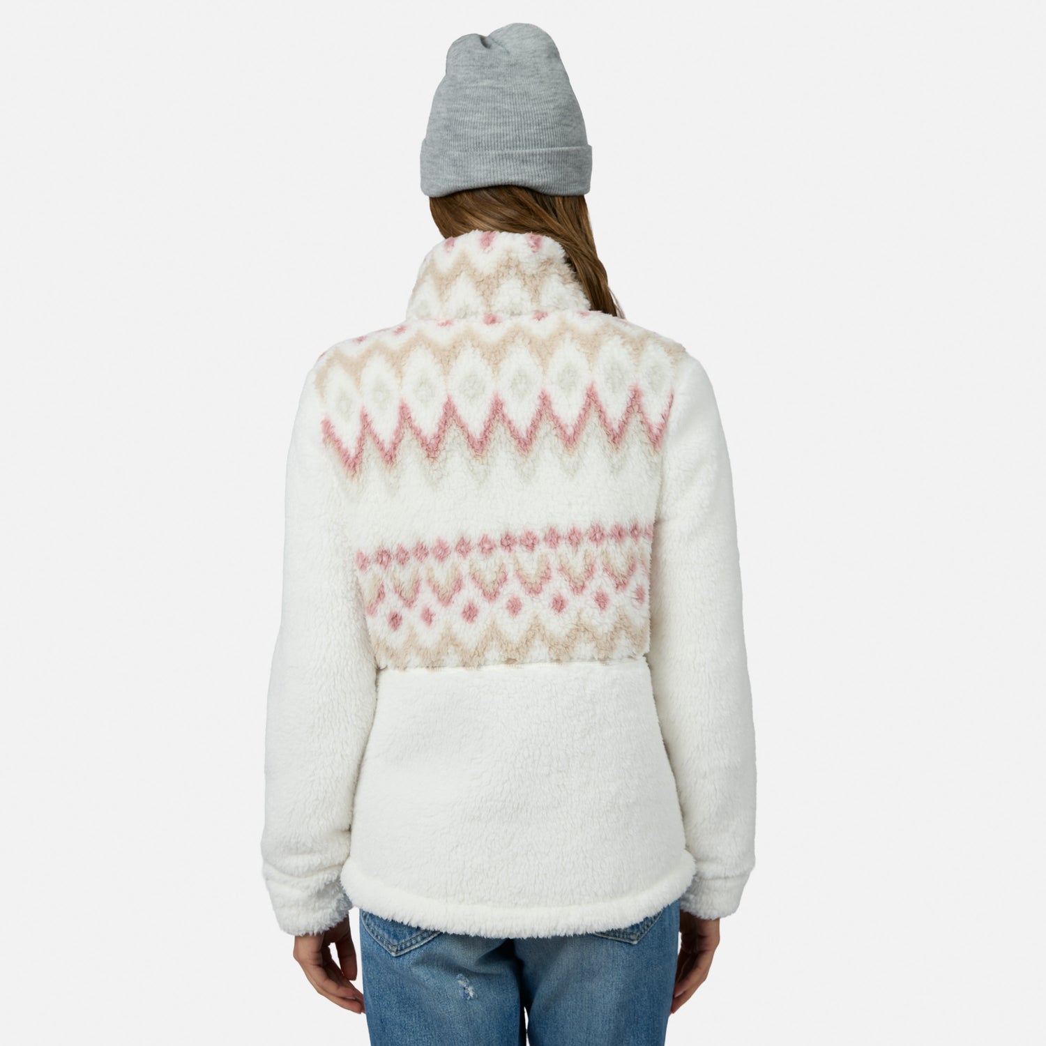 A person in a gray beanie and blue jeans models the Free Country Women’s Sierra Butter Pile® Zip Up Jacket, showcasing its cozy, lightweight warmth and stylish white and pink pattern against a plain white background.