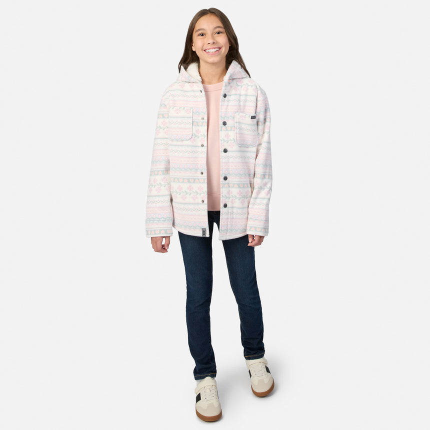 A girl wearing a Free Country Girls’ Chill Out Fleece Shirt Jacket in a plaid print with sherpa lining, a pink long-sleeve shirt, dark blue jeans, and sneakers.