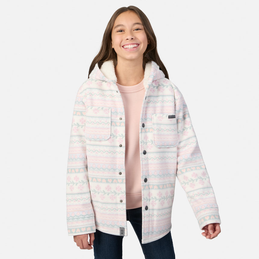 A smiling girl wearing a Free Country Girls’ Chill Out Fleece Shirt Jacket featuring a pink and teal geometric pattern over a light pink shirt.