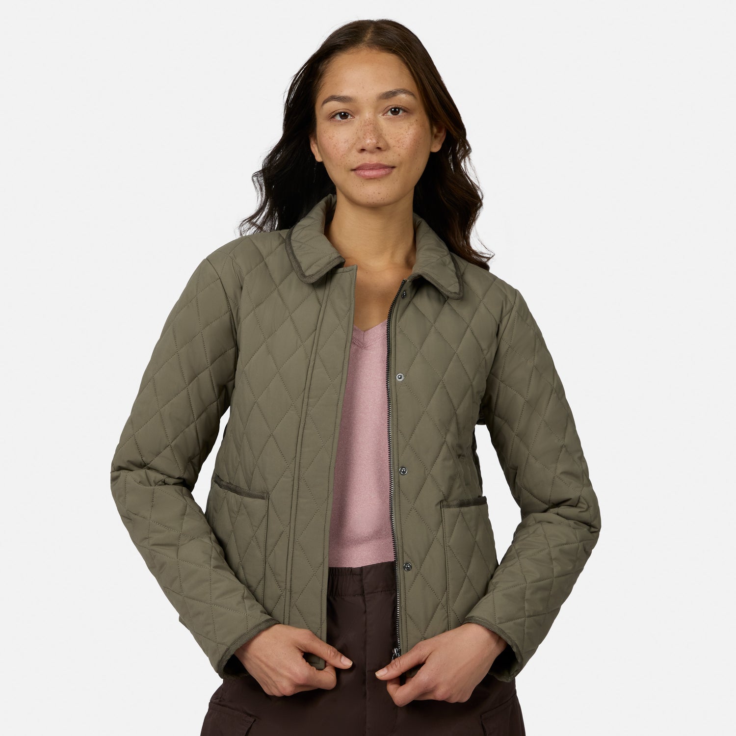 [Model is wearing size S.] A woman modeling a quilted olive green jacket over a dusty pink top and dark brown pants, photographed against a clean light gray studio background.