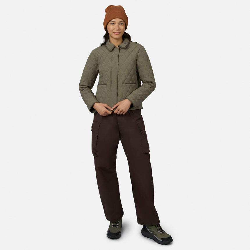 [Model is wearing size S.] A model wearing a quilted olive green jacket, dark brown cargo pants, a rust-colored beanie, and hiking boots, standing against a light gray studio background.
