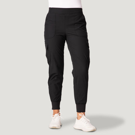 A woman wears Free Country’s Women’s Get Out There Fleece Lined Jogger in black, paired with a white top and white sneakers, standing facing forward against a light gray background.