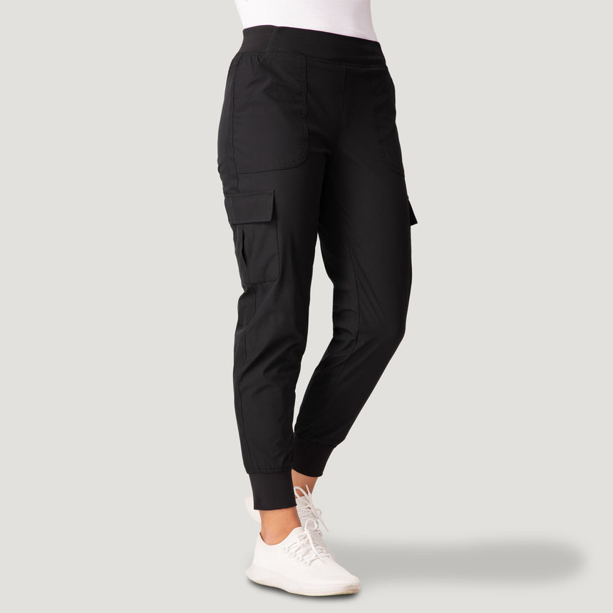 A woman in Free Country’s Women’s Get Out There Fleece Lined Jogger and white sneakers stands against a light gray backdrop. The joggers feature side pockets, ribbed cuffs, and offer warmth and comfort.