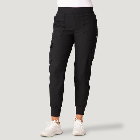 A woman in black Free Country Women’s Get Out There Fleece Lined Jogger with front and side pockets and ribbed cuffs pairs them with white sneakers, standing against a plain light gray background.
