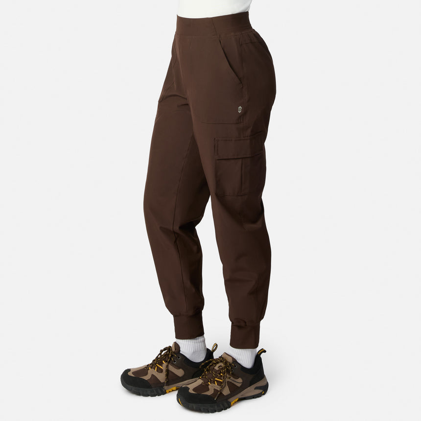 A woman wears the Free Country Women’s Get Out There Fleece Lined Jogger with side pockets and an elastic waistband, paired with camo sneakers, standing against a plain white background.