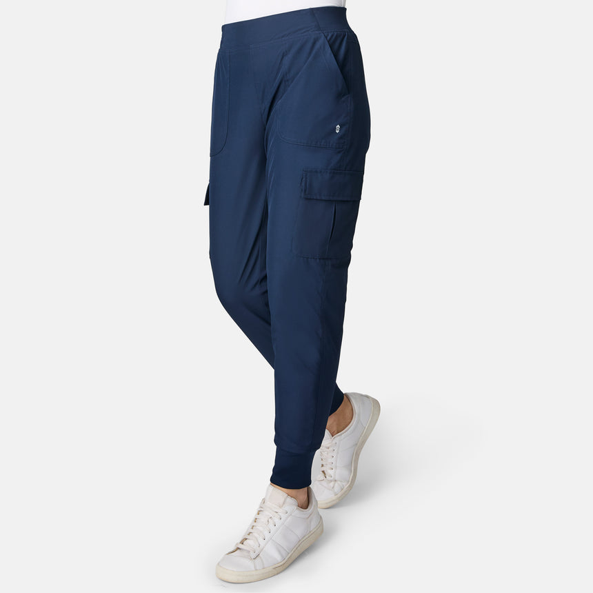 Woman wearing Free Country Women’s Get Out There Fleece Lined Jogger in Midnight with side pockets and white sneakers, standing against a plain white background.