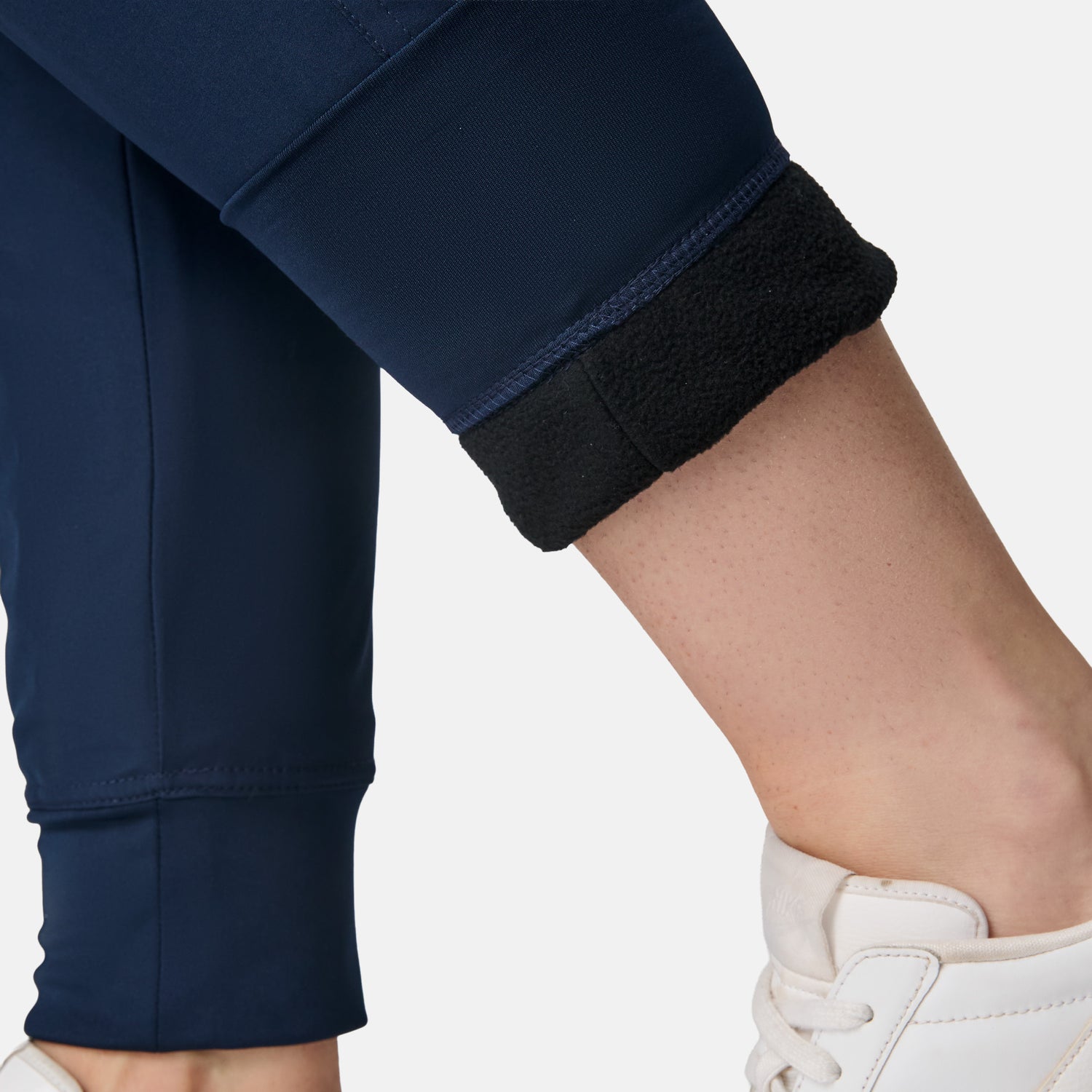 Close-up of a person wearing Free Country Women’s Get Out There Fleece Lined Jogger in navy blue, one leg rolled up to show the black fleece lining, paired with white sneakers.