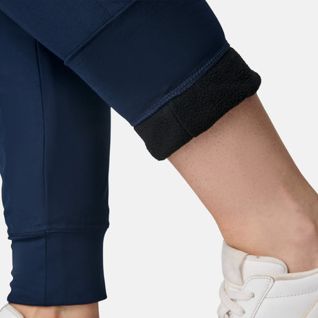 Close-up of a person wearing Free Country Women’s Get Out There Fleece Lined Jogger in navy blue, one leg rolled up to show the black fleece lining, paired with white sneakers.