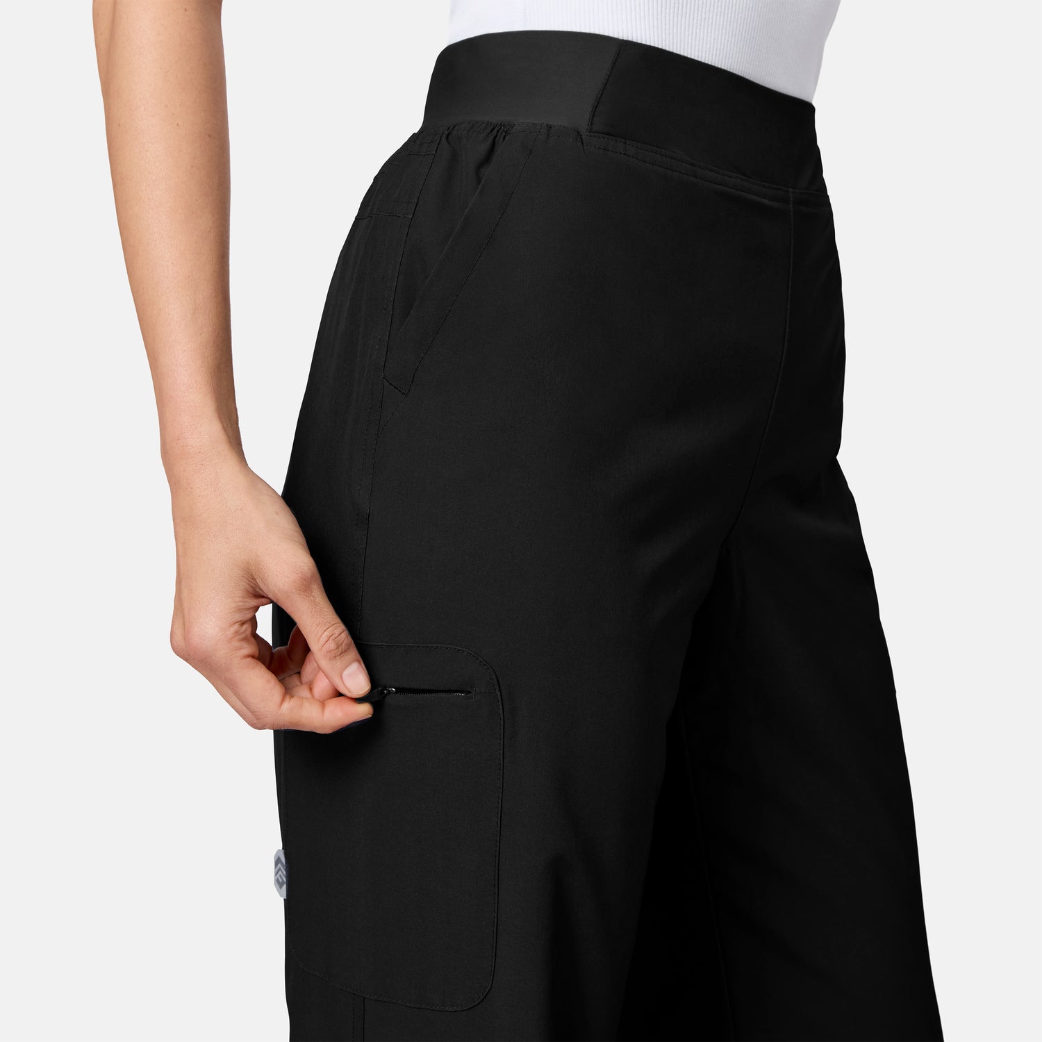 [Model is wearing size S.] Close-up of a person wearing black wide-leg cargo pants, showing the side pocket and hand adjusting the zipper, against a light gray studio background.