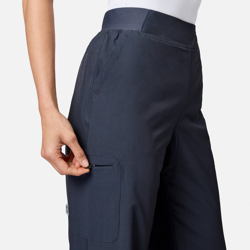 A person wearing Free Country Women’s Get Out There Fleece Lined Pants in dark blue and a white top is shown from the waist down, unzipping a small side pocket on their water-resistant stretch woven pants.