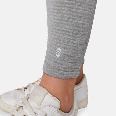 Close-up of a woman's lower leg in Free Country Women's Force Grid Fleece Base Layer Bottoms, light grey with a four-way stretch and small white logo, paired with white sneakers on a plain background.