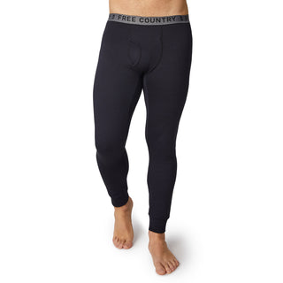 A man stands barefoot on a white background wearing Free Country Men's Force Grid Fleece Base Layer Bottoms in black, featuring a branded waistband and four-way stretch for comfort.