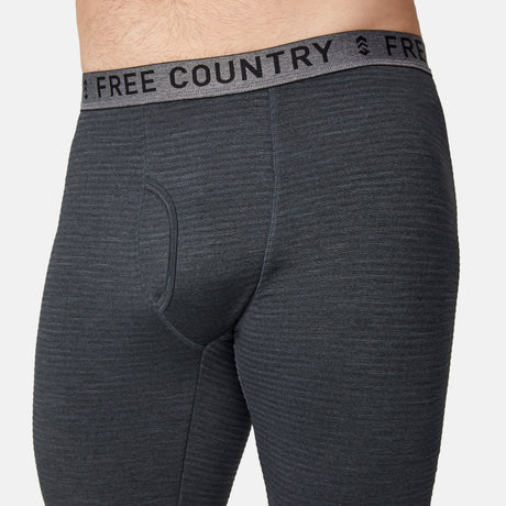 Close-up of a person wearing Free Country Men's Force Grid Fleece Base Layer Bottoms in dark gray, featuring a textured design and branded waistband, covering the lower torso and upper legs against a plain background.
