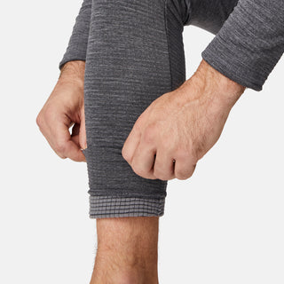 A man in Free Country’s Men's Force Grid Fleece Base Layer Bottom rolls up one pant leg, revealing its four-way stretch fleece and an additional gray textured fabric layer underneath.