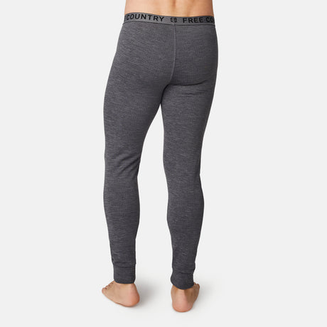 A person stands barefoot facing away, wearing Free Country Men's Force Grid Fleece Base Layer Bottoms—gray thermal leggings with a black FREE COUNTRY waistband and four-way stretch—for comfort. The background is plain white.