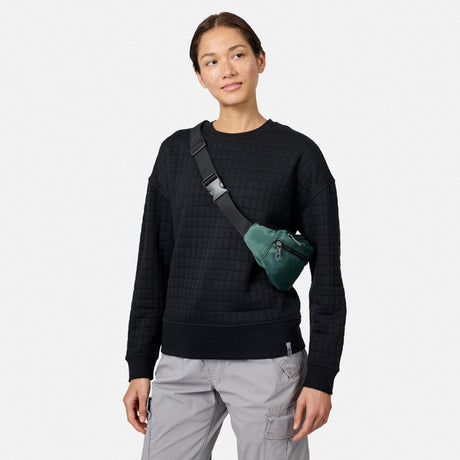 A woman in a black Free Country Women’s UltraFill Fleece Crew Neck Pullover Top and light gray cargo pants faces forward, wearing a green crossbody bag and gazing slightly to the side against a plain white background.