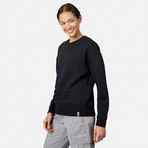 A person smiles in a black Women’s UltraFill Fleece Crew Neck Pullover Top by Free Country, paired with light gray cargo pants, standing against a plain white background.