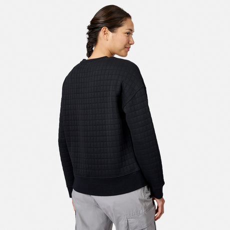 A woman with dark braided hair models the Free Country Women’s UltraFill Fleece Crew Neck Pullover Top and light gray pants. She faces away, looking over her shoulder, against a plain white background.