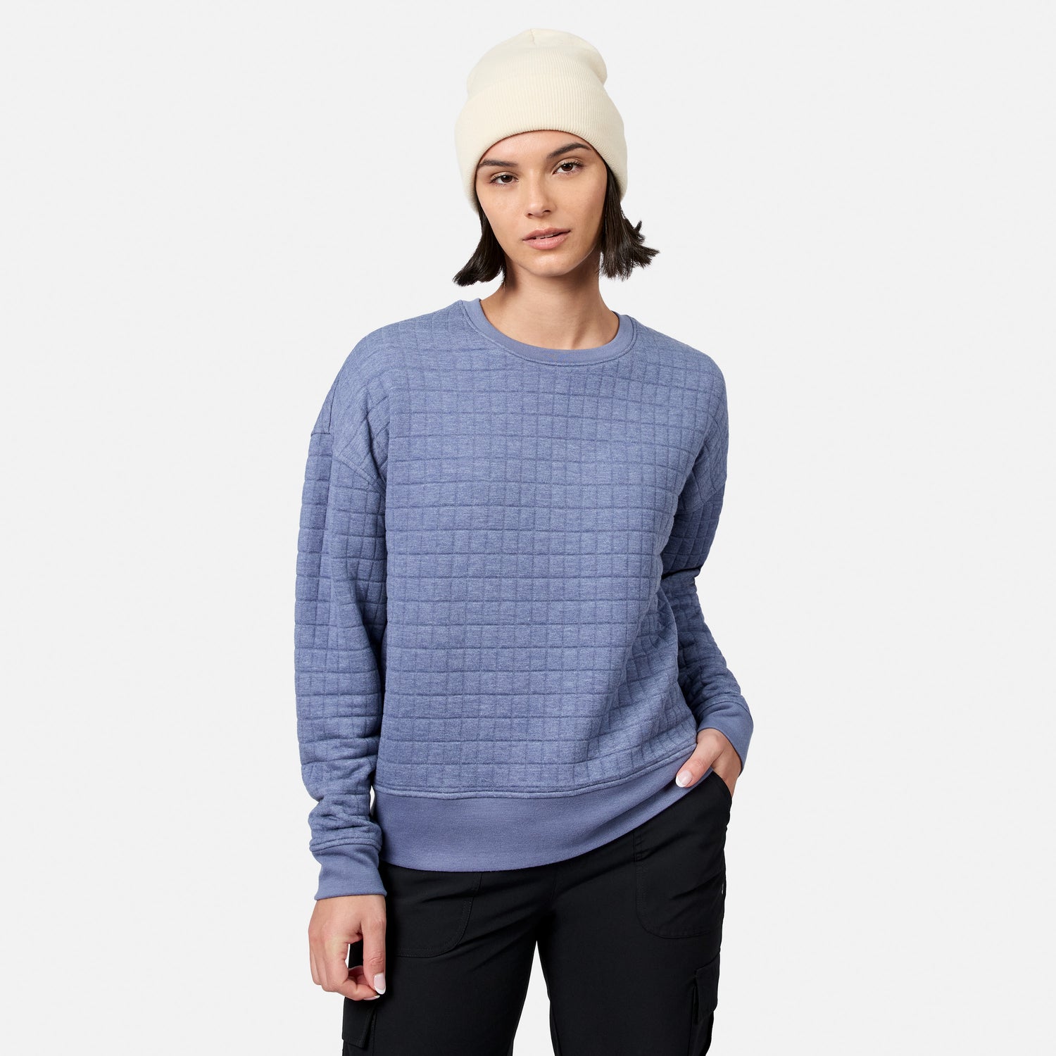 Wearing Free Country’s Women’s UltraFill Fleece Crew Neck Pullover Top in textured light purple, paired with a white beanie and black pants, the person stands against a plain light gray background.
