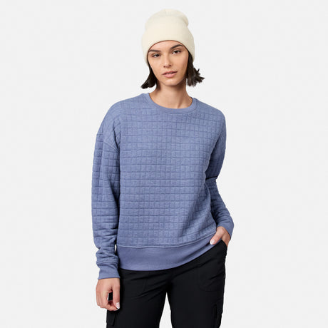 Wearing Free Country’s Women’s UltraFill Fleece Crew Neck Pullover Top in textured light purple, paired with a white beanie and black pants, the person stands against a plain light gray background.