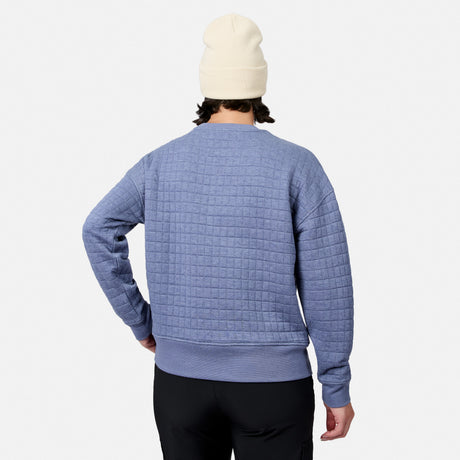 A person in a cream beanie, black pants, and a light blue Free Country Women’s UltraFill Fleece Crew Neck Pullover Top stands facing away from the camera against a white background.