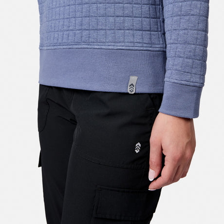 A person wears a Free Country Women’s UltraFill Fleece Crew Neck Pullover Top in blue and black cargo pants, shown from the waist down with one hand relaxed at their side against a plain white background.