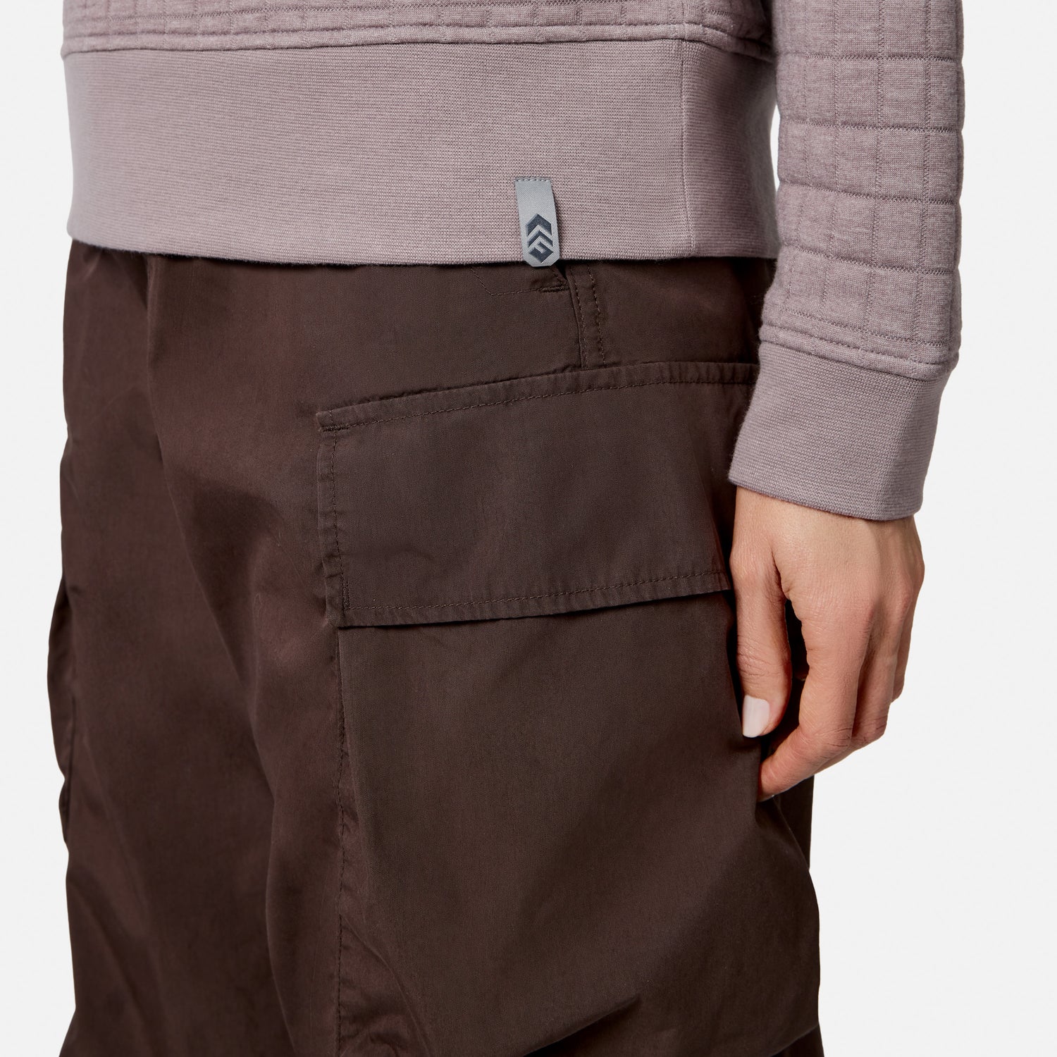 A person wears a textured, light purple Free Country Women’s UltraFill Fleece Crew Neck Pullover Top and brown cargo pants, with one hand resting by their side near the large pocket.