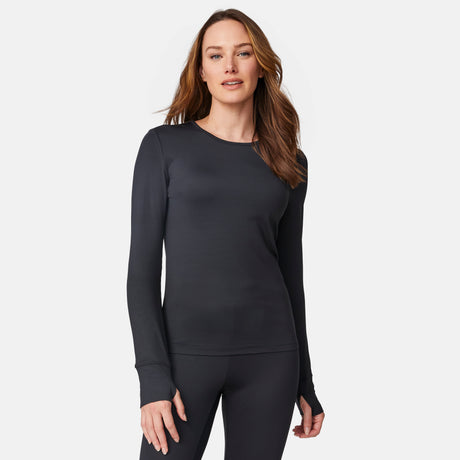 A woman with long brown hair is wearing the Free Country Women’s Microtech® Heat Cocarber® Coffee Base Layer Top 2-Pack in black, featuring a fitted, long-sleeve design made from moisture-wicking recycled materials, standing against a plain white background.