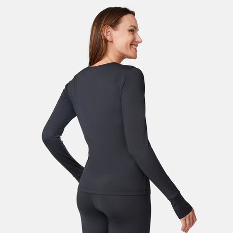 Wearing a fitted, long-sleeve black Women’s Microtech® Heat Cocarber® Coffee Base Layer Top by Free Country, she stands facing away in matching leggings made from recycled materials, looking over her shoulder and smiling.