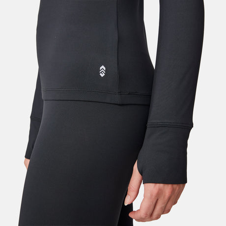 A person wearing the Free Country Women’s Microtech® Heat Cocarber® Coffee Base Layer Top, crafted from recycled materials with a small white logo near the waist and thumb holes at the sleeve cuffs.