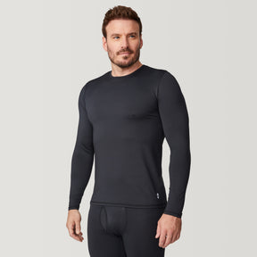 A man wearing the Free Country Men’s Microtech® Heat Cocarber® Coffee Base Layer Top in black, along with matching black leggings made from recycled materials, stands against a plain light background, looking slightly to the side.