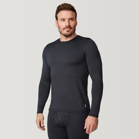 A man wearing the Free Country Men’s Microtech® Heat Cocarber® Coffee Base Layer Top in black, along with matching black leggings made from recycled materials, stands against a plain light background, looking slightly to the side.