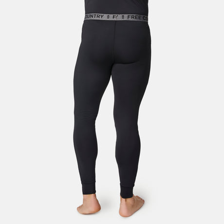 A man stands barefoot, facing away, wearing black fitted Men’s Microtech® Heat Cocarber® Coffee Base Layer Bottoms by Free Country, with the brand name displayed on the waistband. Made from recycled materials, these base layers offer moisture-wicking and anti-odor protection. The background is plain white.
