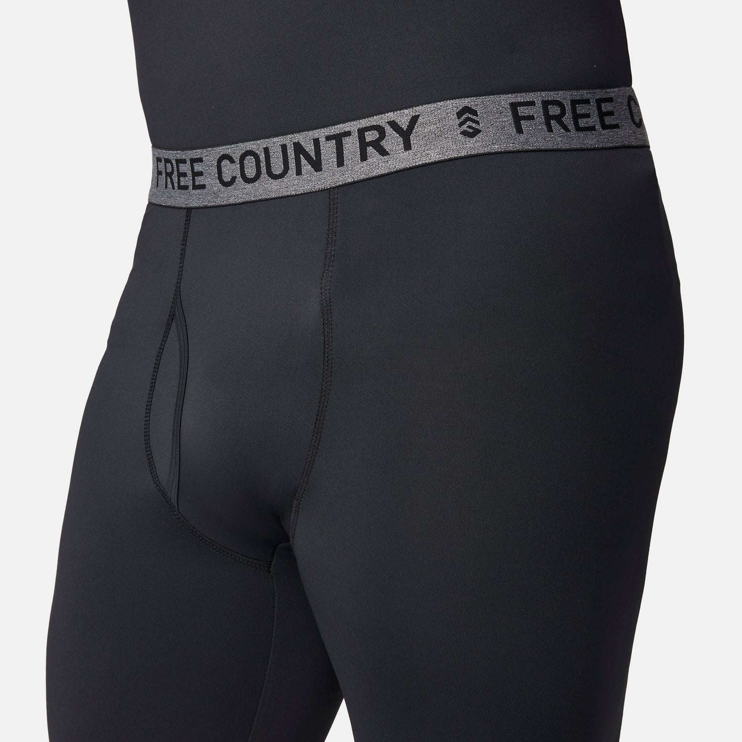 Close-up of a person wearing Free Country Men’s Microtech® Heat Cocarber® Coffee Base Layer Bottoms, featuring black athletic leggings with a gray waistband that reads FREE COUNTRY in bold letters. Designed with four-way stretch for optimal comfort, the focus is on the waistband and upper part of these performance base layer bottoms.