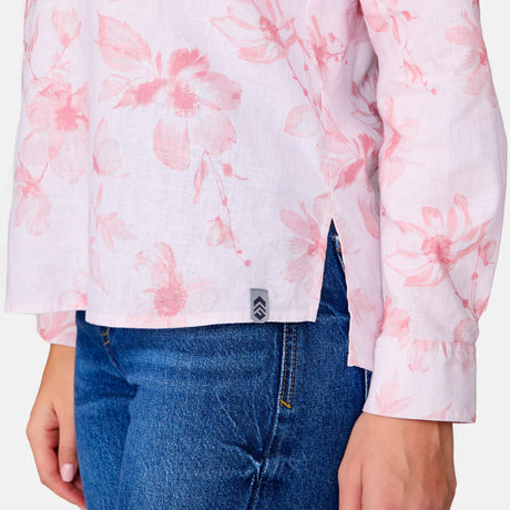 A person is shown from torso to upper legs wearing blue jeans and the Clearance Women's Easy Breezy Long Sleeve Shirt—a light pink floral cotton-linen blend top with a V-neck, side slits, roll-up sleeves, and a small gray hem tag.