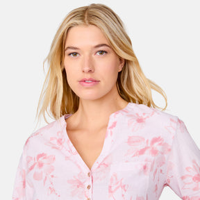 A woman with long blonde hair models the Clearance Women's Easy Breezy Long Sleeve Shirt in light pink with a floral print and adjustable roll-up sleeves, standing before a plain gray background and gazing neutrally at the camera.