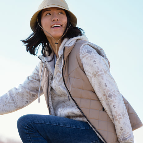 Woman wearing a beige quilted vest with a patterned design, sitting outdoors.