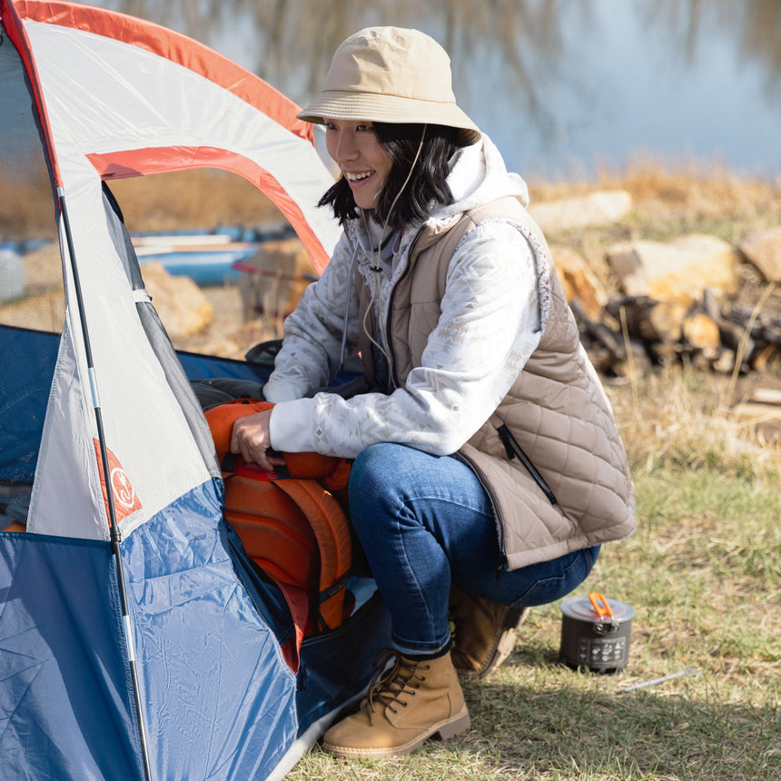 Person sitting by a tent in an outdoor setting with a lake in the background