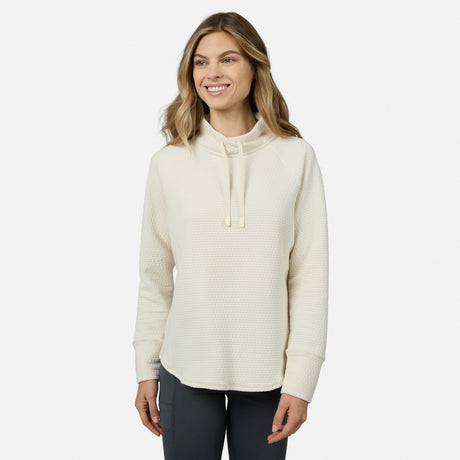 A smiling woman wears a cream-colored Free Country Women’s UltraFill Cowl Neck Top featuring a textured, seamless quilting pattern and a drawstring.