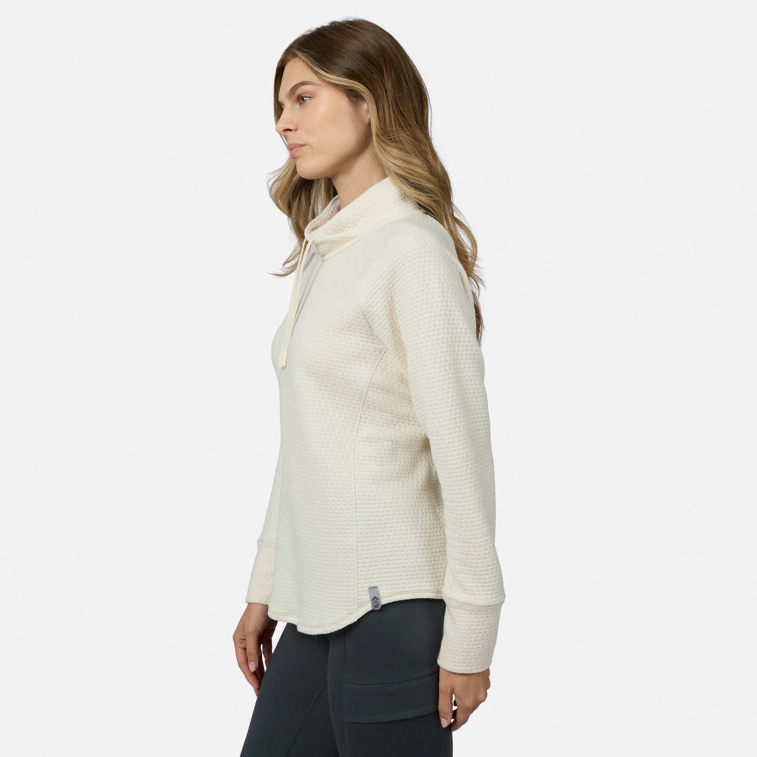 Side profile of a woman wearing a cream-colored, long-sleeved Free Country Women’s UltraFill Cowl Neck Top with a textured, seamless quilting finish.