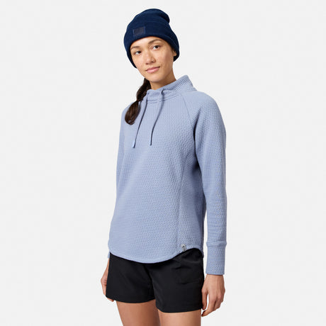 A woman wearing a periwinkle blue textured Women’s UltraFill Cowl Neck Top, black shorts, and a navy blue beanie.