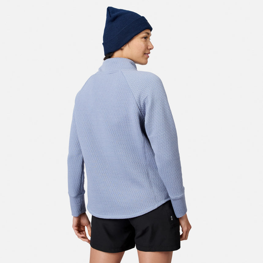 A person wearing a blue textured Free Country Women’s UltraFill Cowl Neck Top, black shorts, and a navy blue beanie.